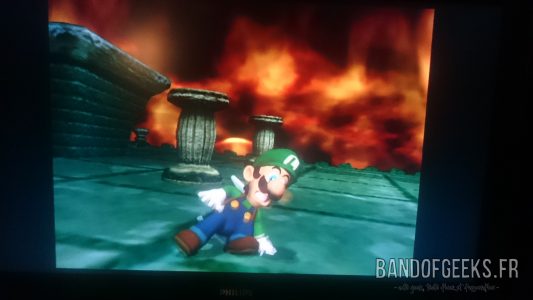 Luigi's Mansion Luigi glisse sur le sol marbré devant un mur de feu